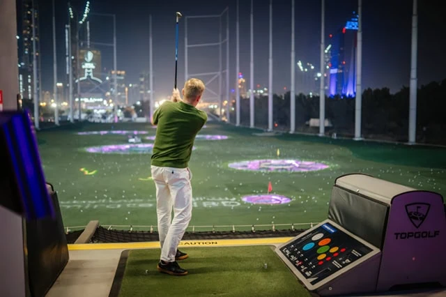 10 Monthly Dividend Stocks for Frequent, Regular Income 23 a man takes a swing at a topgolf facility in Dubai.
