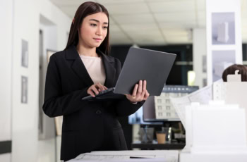 A young architect holds her laptop while standing.