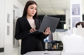 A young architect holds her laptop while standing.