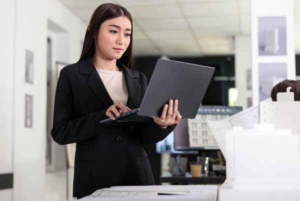 A young architect holds her laptop while standing.