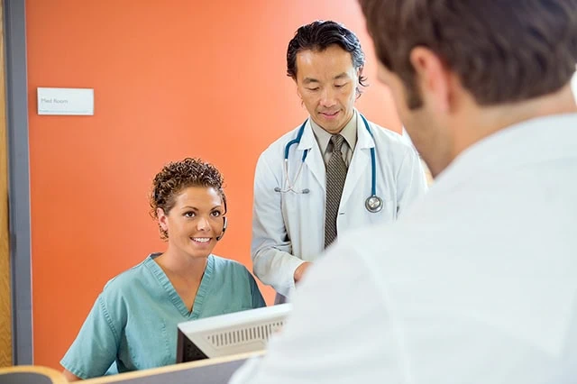 a nurse receptionist and a doctor in an office with a very orange wall.