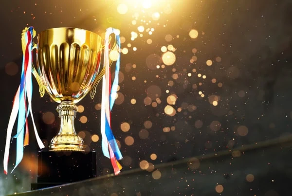 a golden trophy with ribbons against a dark background with shining gold light spots.