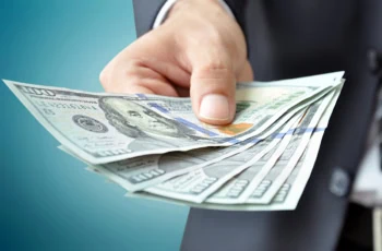 a man in a business suit holds out several hundred dollar bills.