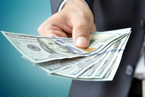 a man in a business suit holds out several hundred dollar bills.