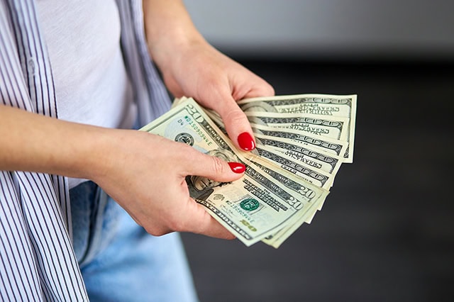 a woman with painted nails fans out numerous 20 dollar bills.