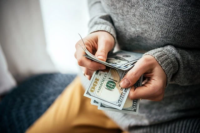 How Retirees Can Master Budgeting With a Variable Income 3 a person in a sweater counts hundred dollar bills.