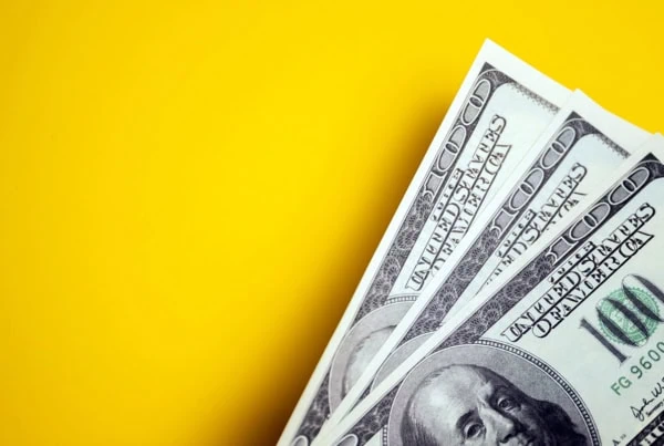 three hundred-dollar bills in front of a yellow background.