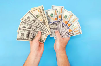 a pair of hands fan out a bunch of old and new hundred dollar bills.