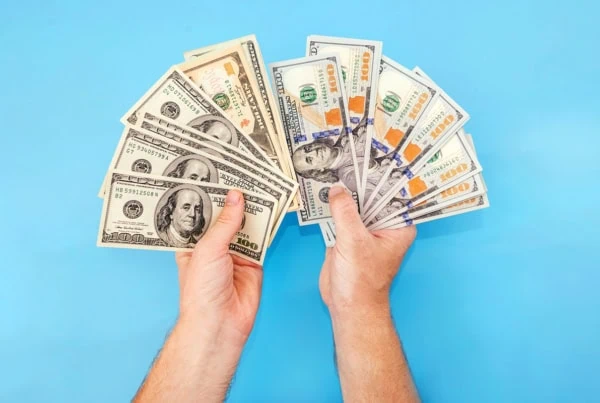 a pair of hands fan out a bunch of old and new hundred dollar bills.