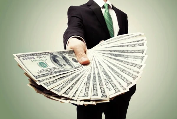 a businessman handing out a fanned out stack of hundred dollar bills.