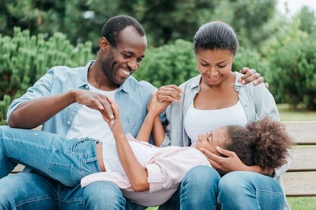 family of three outdoors on bench smiling