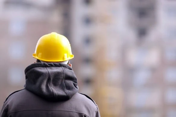 a man wearing a hoodie and construction helmet looks away from the camera.