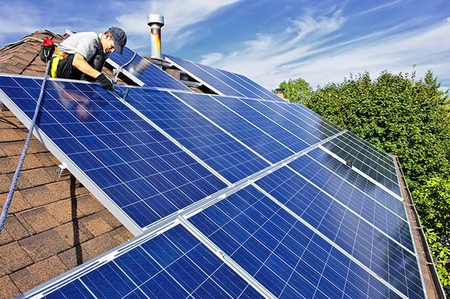 workers install solar panels on a roof.