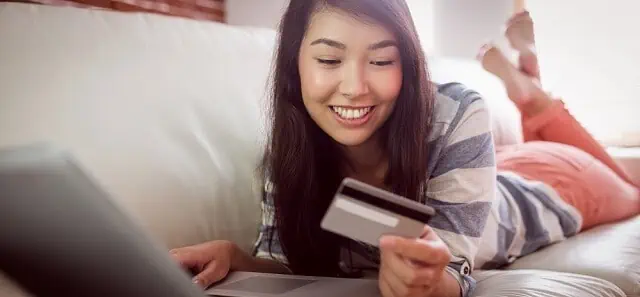 girl on couch with card and laptop smiling