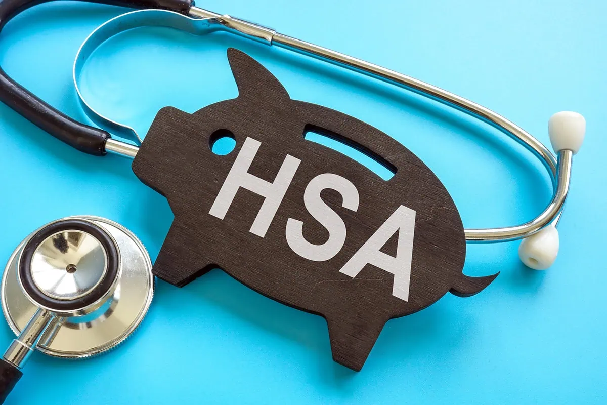 Health Savings Accounts (HSAs) vs. Flexible Spending Accounts (FSAs): What Are the Differences? 2 a stethoscope wrapped around a flat wooden piggy bank carving that says H S A.