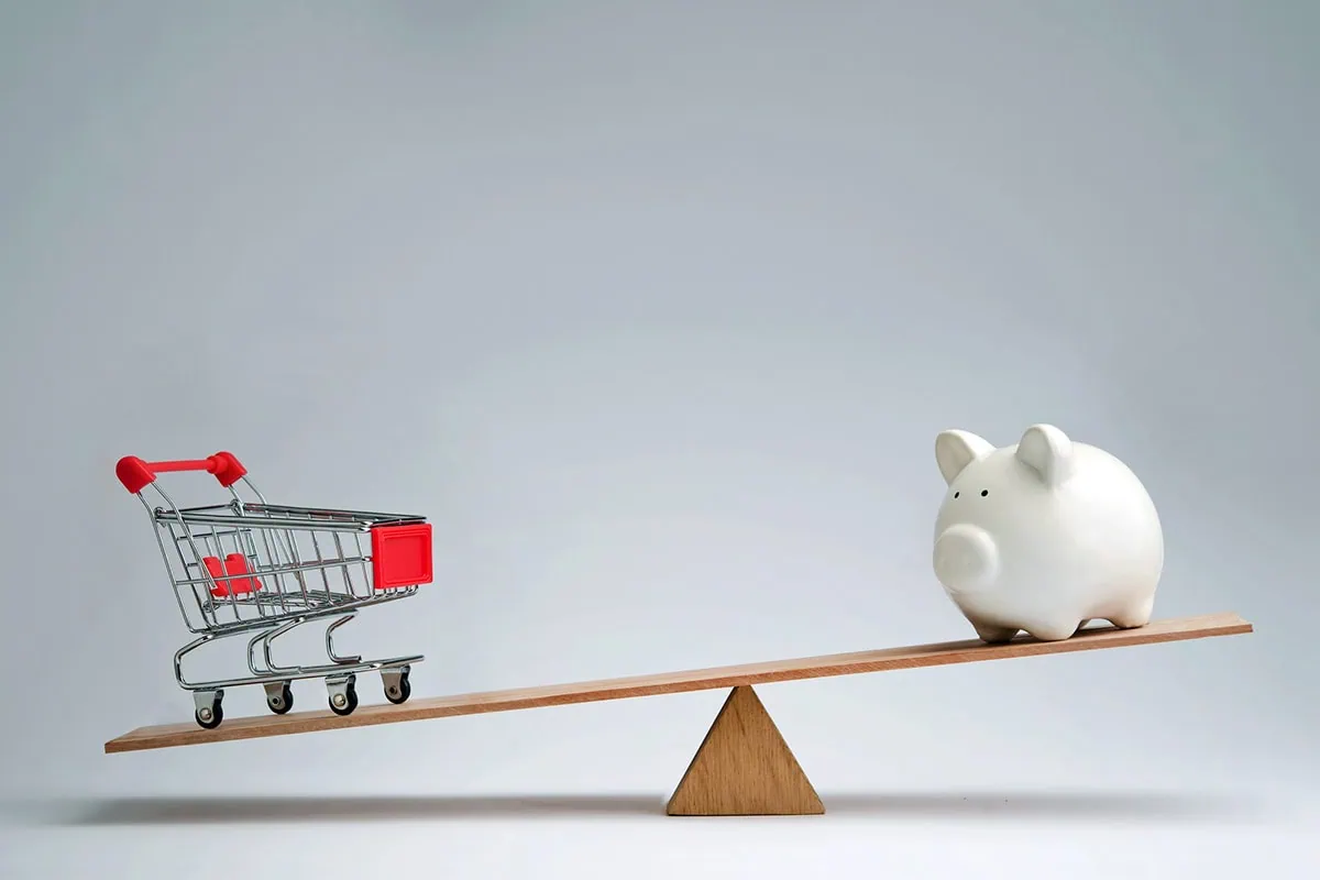 a piggy bank and a shopping cart are on opposite sides of a seesaw.