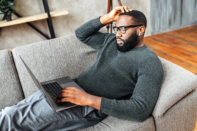 The Quick Guide to Rebalancing Your Portfolio 13 a black man in his 30s rests on a couch while using his laptop.