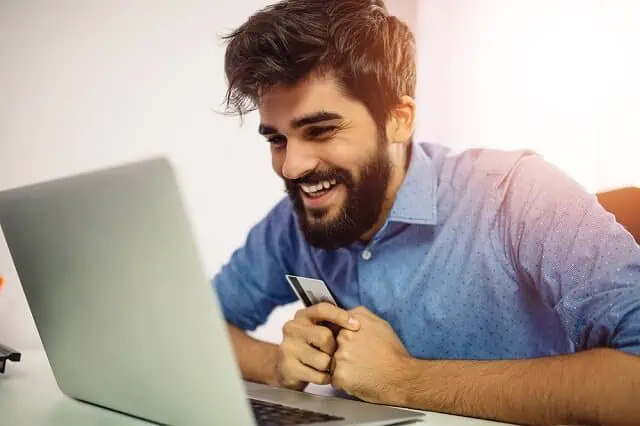 man smiling at computer with credit card in hand