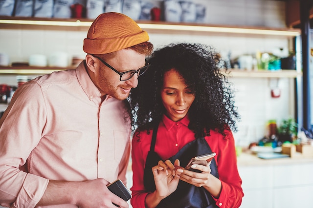 Positive guy together with cheerful waitress watching funny video on website on smartphone