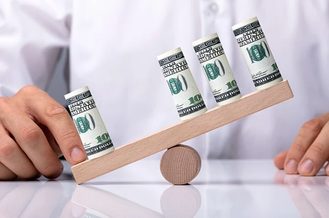 Human Hand Showing Unbalance Between Rolled Up dollars On Seesaw