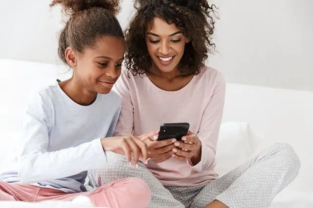 mother and daughter on bed smiling while looking at smartphone