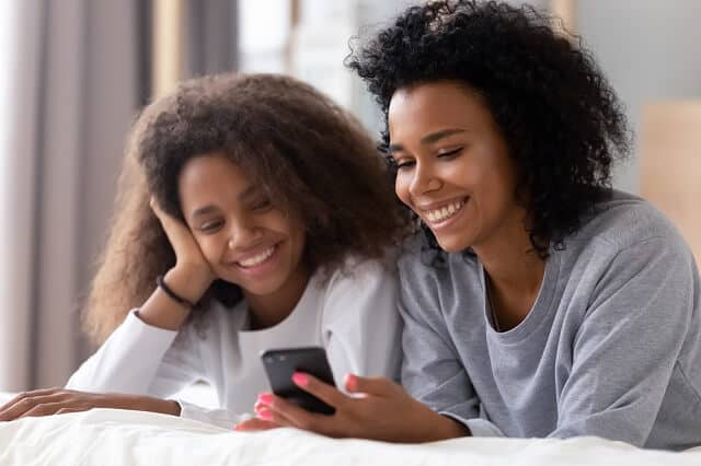 mother and daughter on bed smiling with smartphone