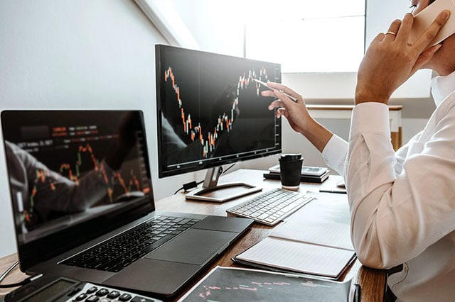 an investor looks at multiple screens showing stock charts.