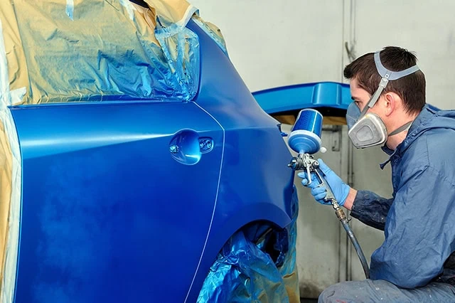 a worker spray-paints a car blue.