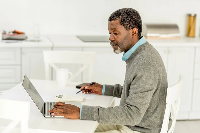 senior man looking at laptop and calculator with pen and paper 640