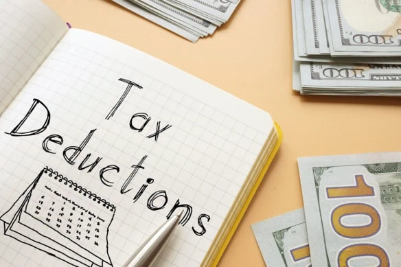 the words tax deductions are written on a notepad sitting on a table with many hundred dollar bills.