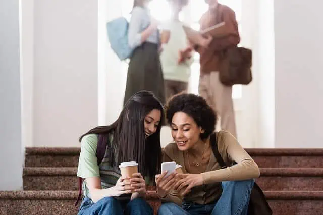 young female students in the hallway on phone with coffee