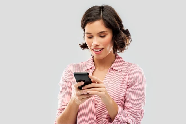 technology and people concept - happy smiling young woman in striped shirt using smartphone over grey background